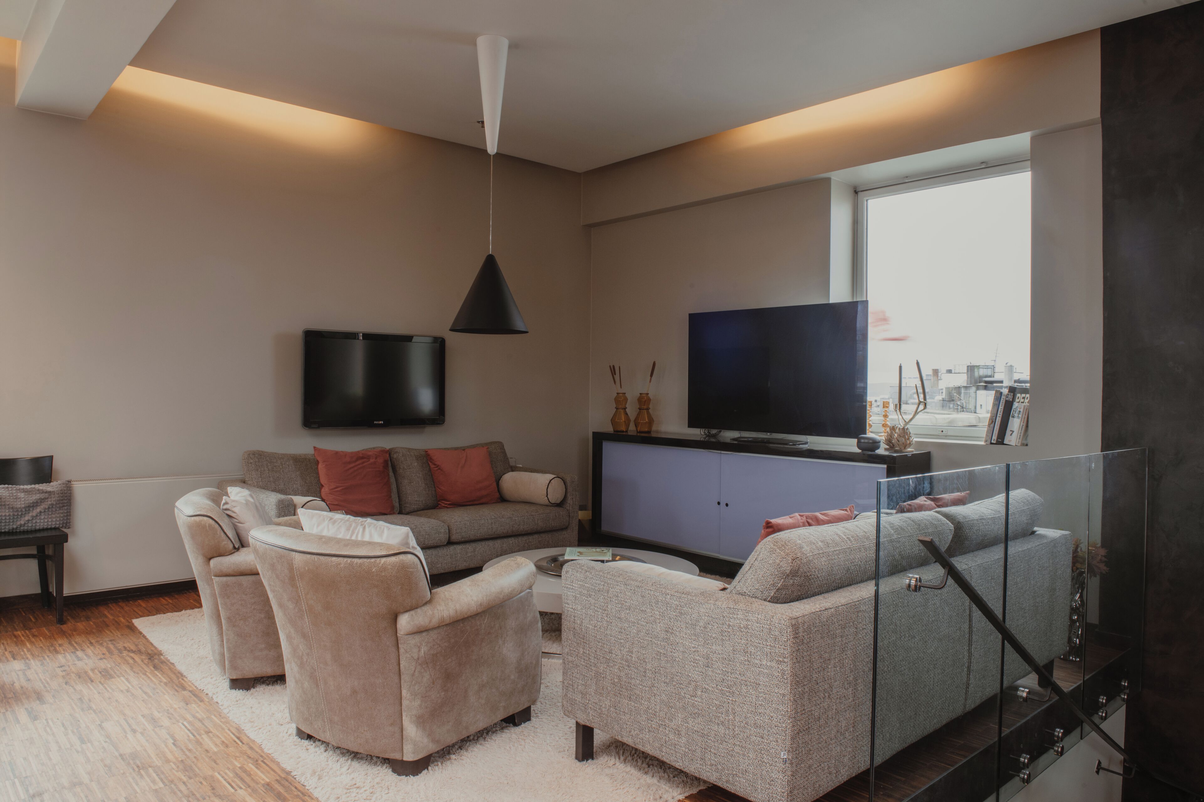 Uma sala de estar moderna com um conjunto de sofás, uma televisão e um guarda-corpo de vidro.