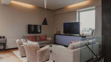 Uma sala de estar moderna com um conjunto de sofás, uma televisão e um guarda-corpo de vidro.