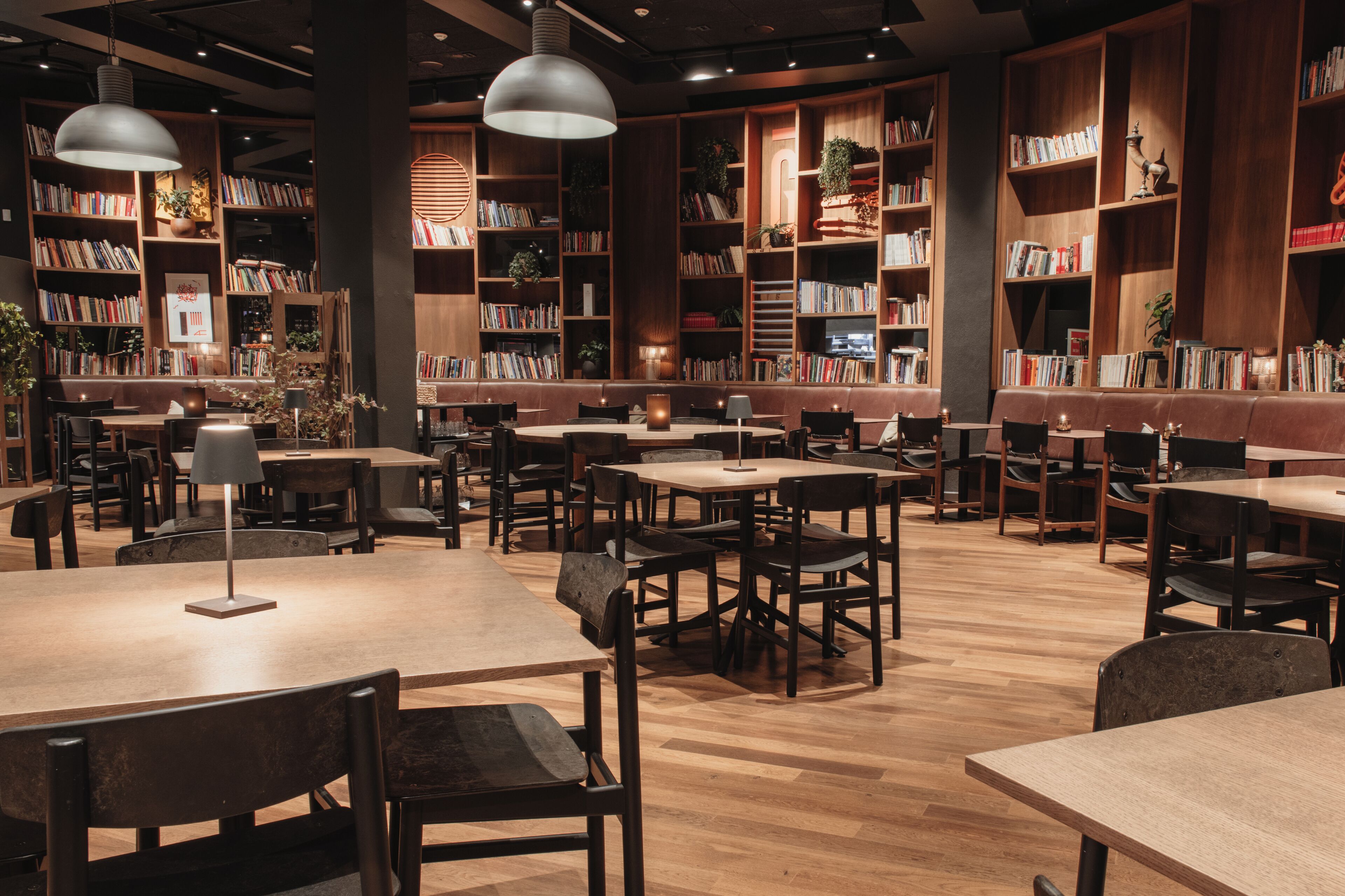 A library with bookshelves, tables, chairs, and pendant lighting.