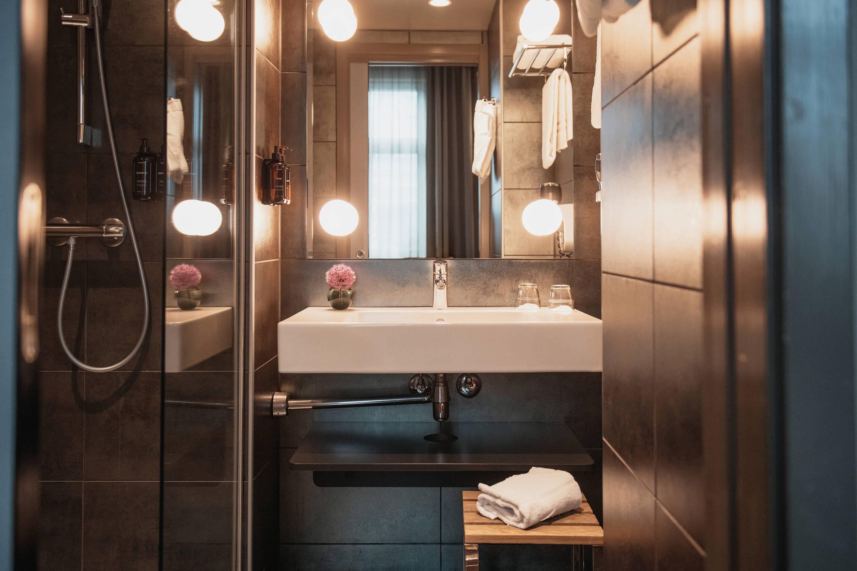 A modern bathroom with a glass shower enclosure, a white sink, and a mirror with lights.