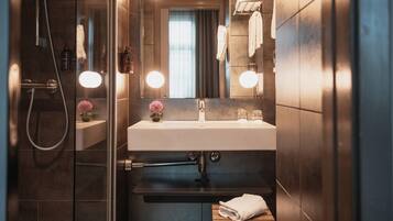 A modern bathroom with a glass shower enclosure, a white sink, and a mirror with lights.