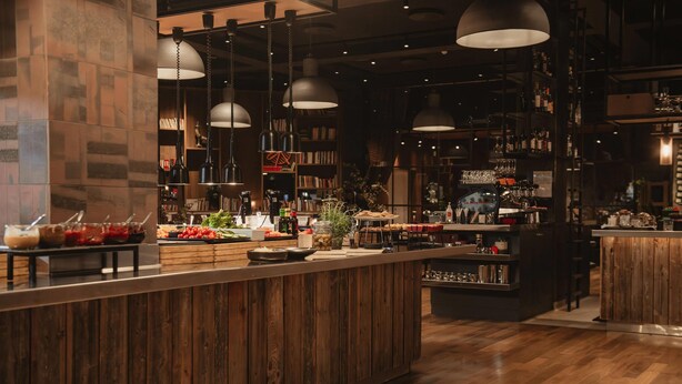 A bar area with wooden counter, hanging pendant lights, and shelves with bottles and glasses. - Home Hotel Folketeateret (Oslo)