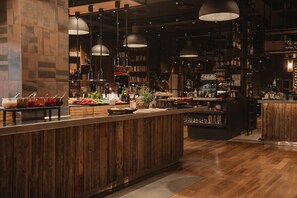 Una zona de bar con mostrador de madera, luces colgantes y estantes con botellas y copas.