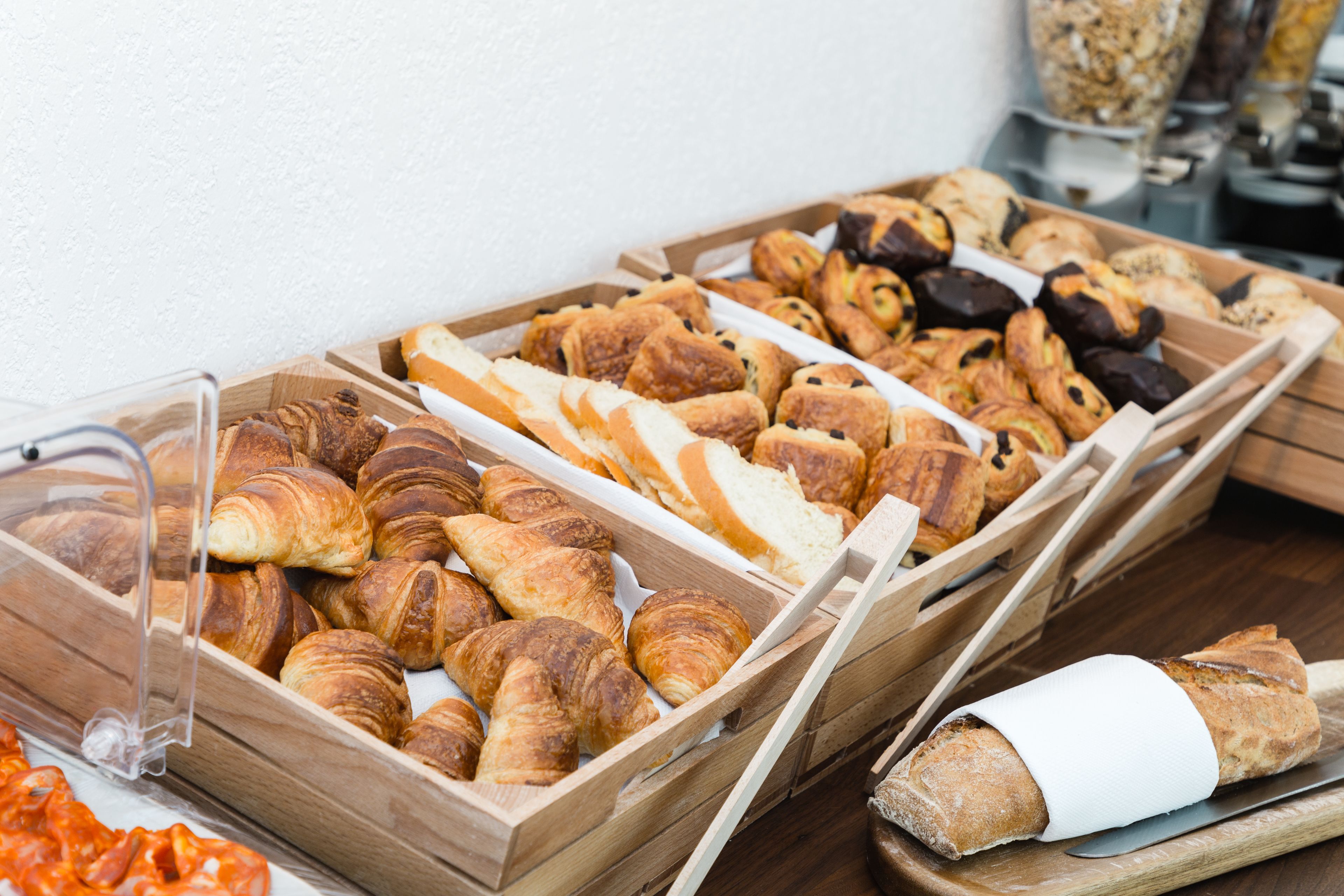 A variety of baked goods displayed in wooden trays, including croissants and bread.