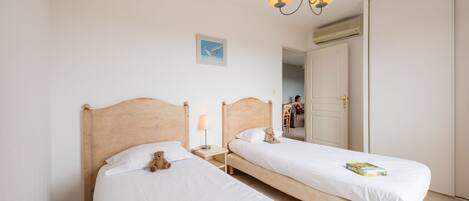 Une chambre d’hôtel avec deux lits simples, une tête de lit en bois, une table de chevet avec une lampe, un luminaire au plafond et un tableau encadré au mur.