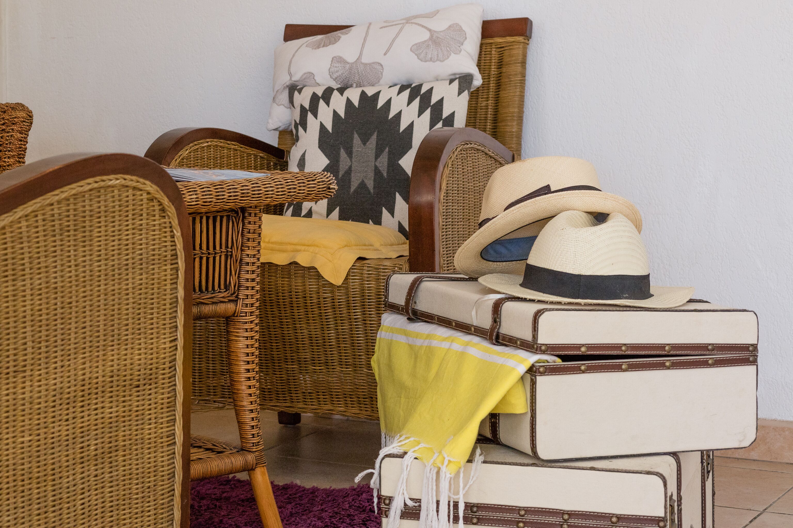 A room with wicker furniture, a patterned pillow, and stacked suitcases.