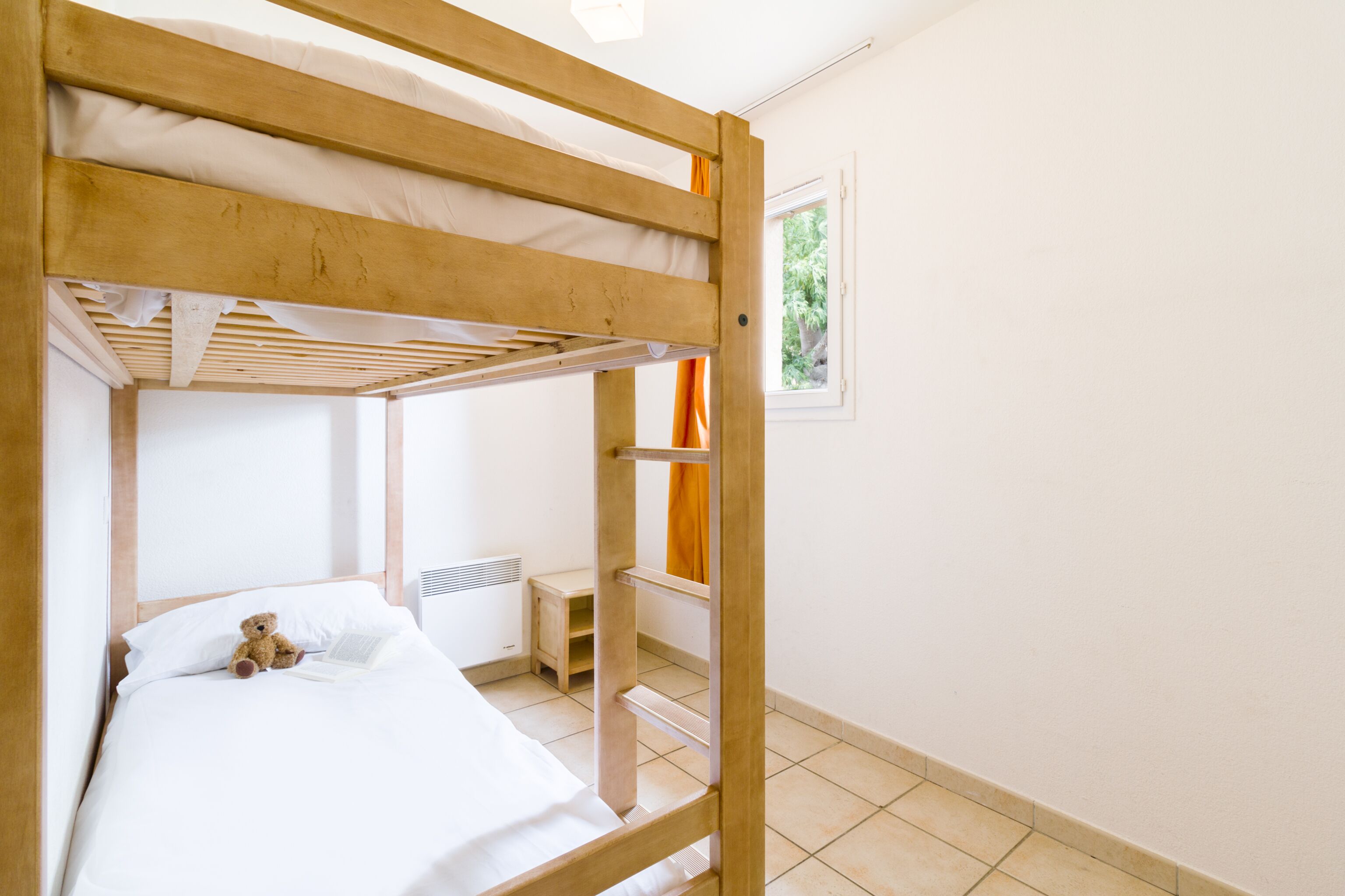 A bunk bed with a white mattress and a teddy bear on the lower bunk.