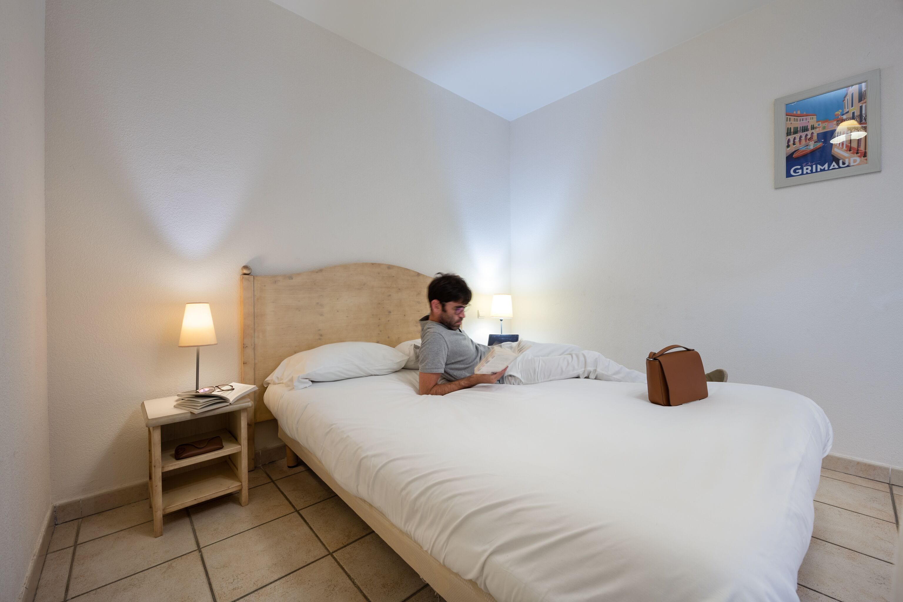 A hotel room with a bed, a nightstand with a lamp, and a poster on the wall.