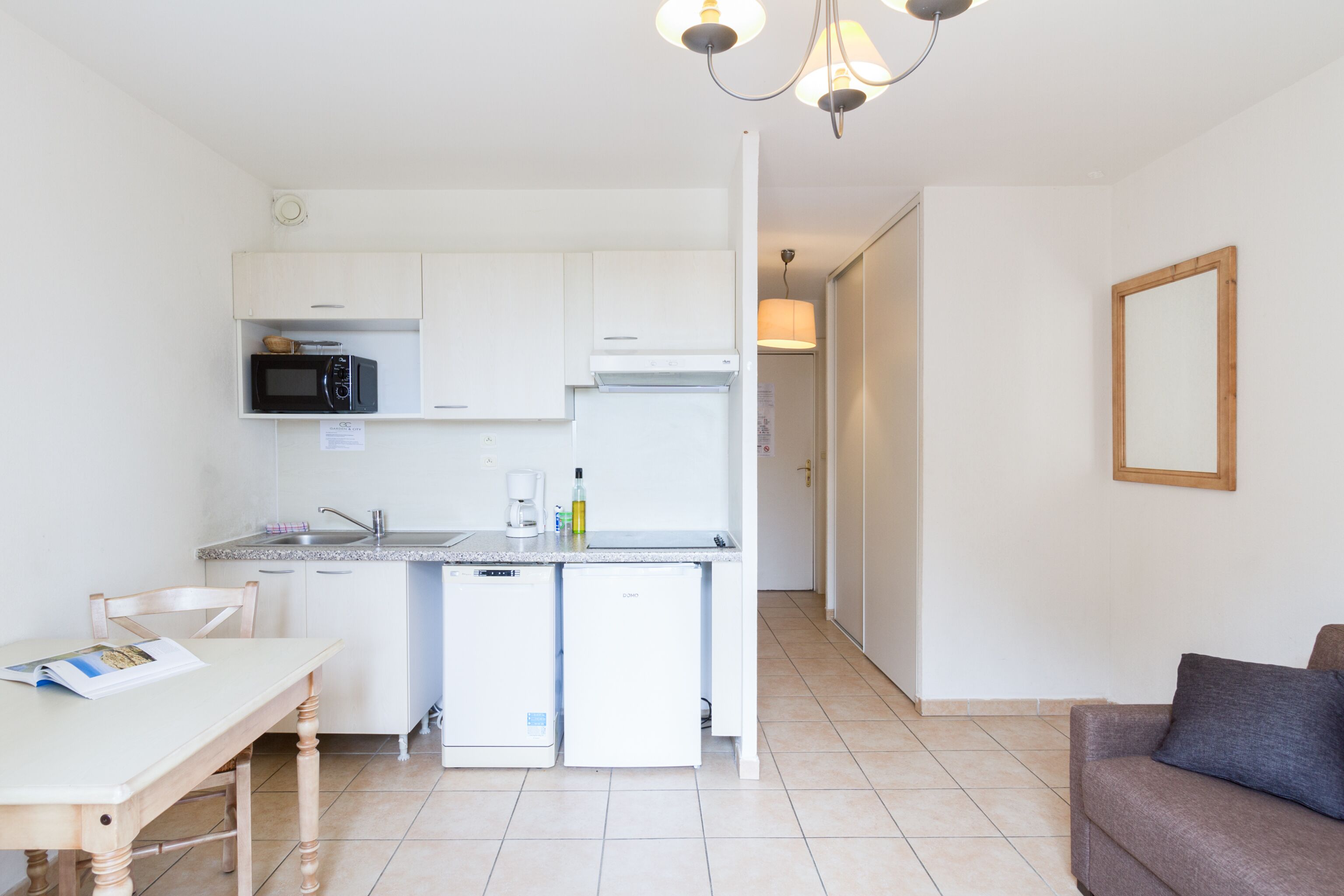 A compact kitchen with white cabinets, a microwave, a coffee maker, and a small refrigerator.