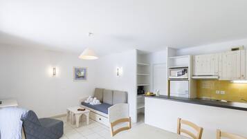A compact living space with a kitchenette, a sofa, a dining table, and a small kitchen counter.