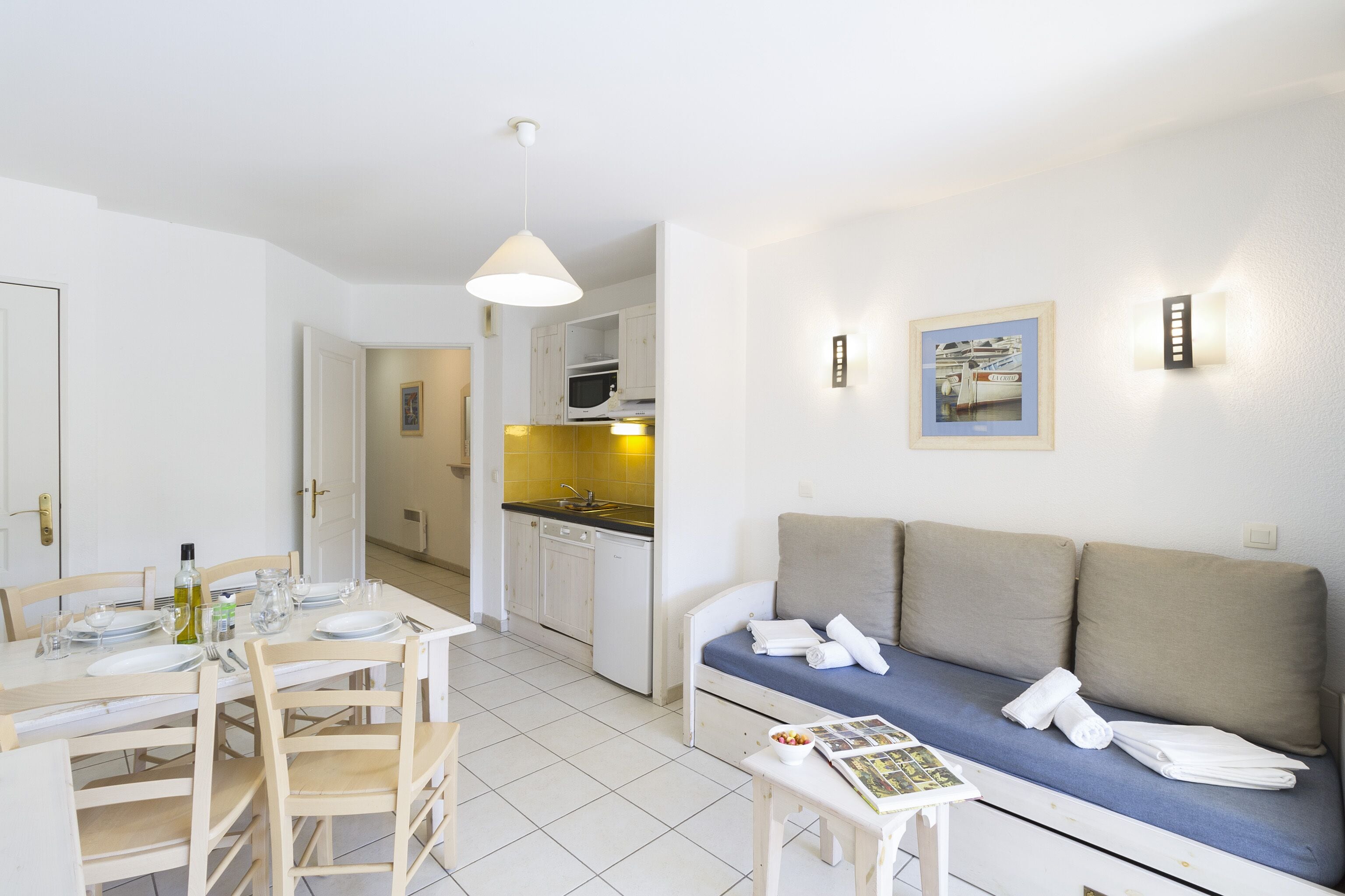 A compact living space with a dining area, kitchenette, and a sofa with towels.