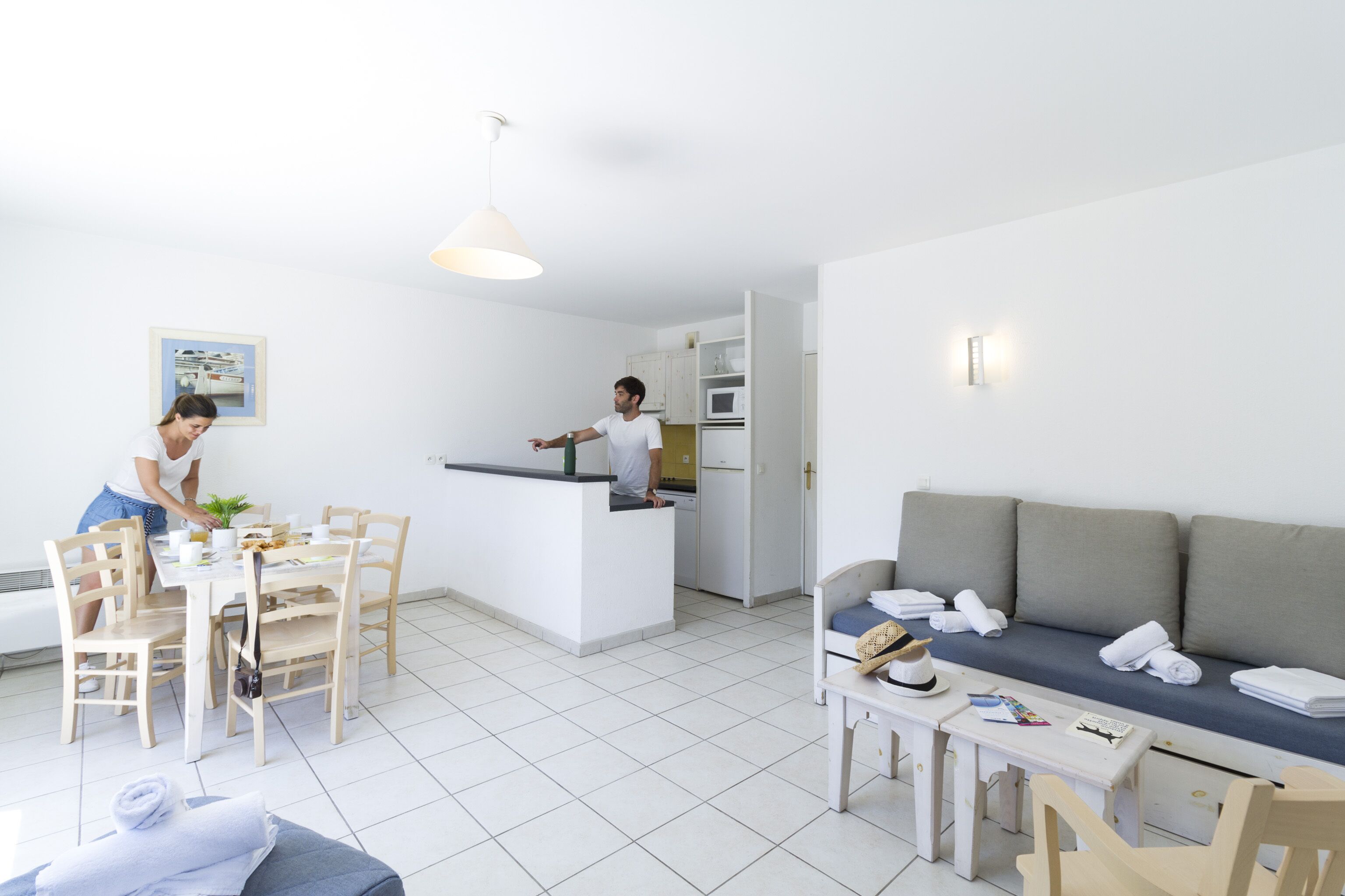 A modern living room with a dining area, a kitchen, and a sofa with towels.