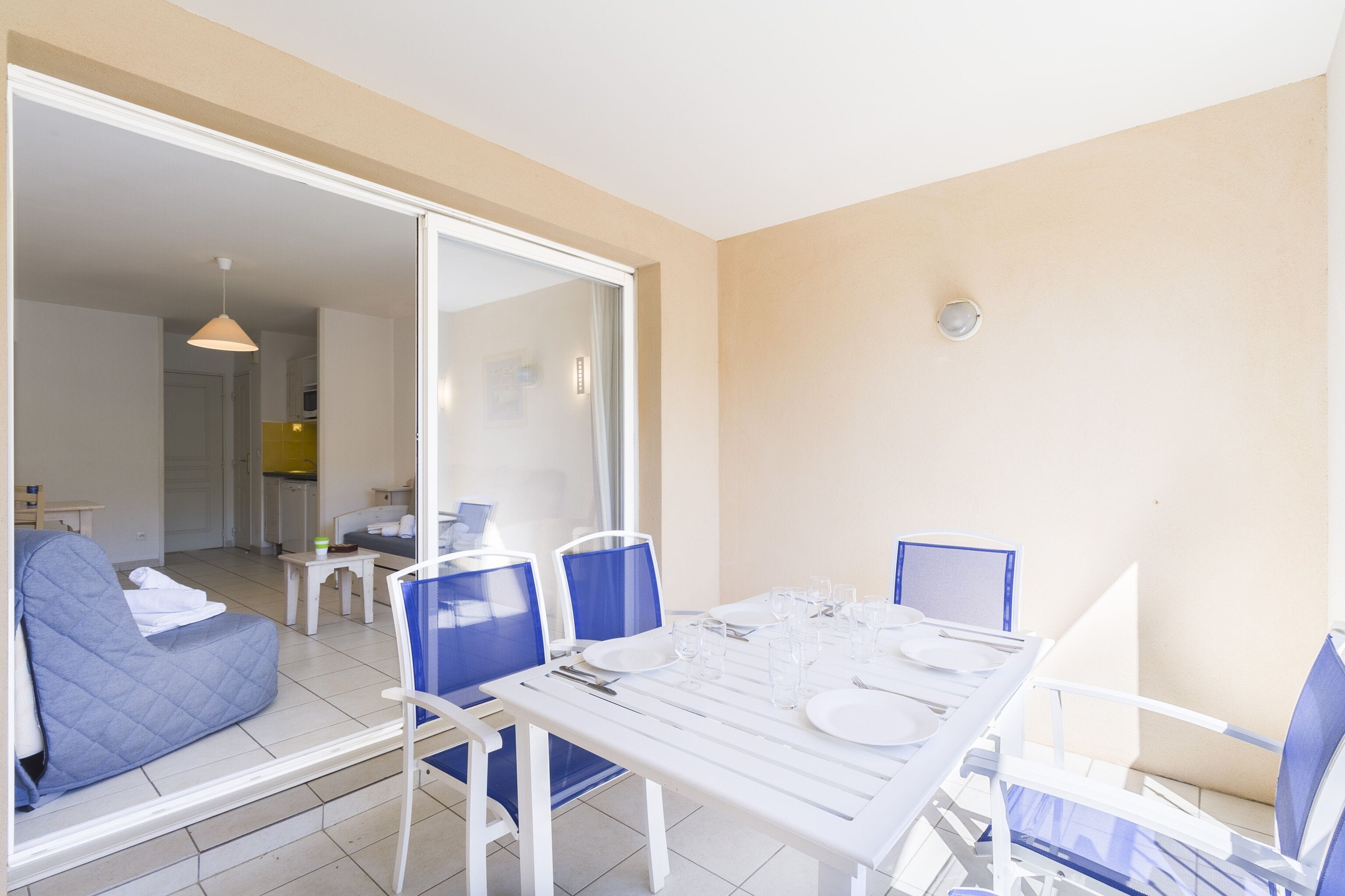 Un coin repas avec une table dressée pour quatre personnes, des chaises bleues et une cloison en verre qui sépare l’espace repas du salon.