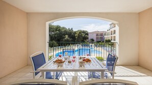Un balcón con una mesa lista para comer, con vistas a una piscina y un edificio con balcones.
