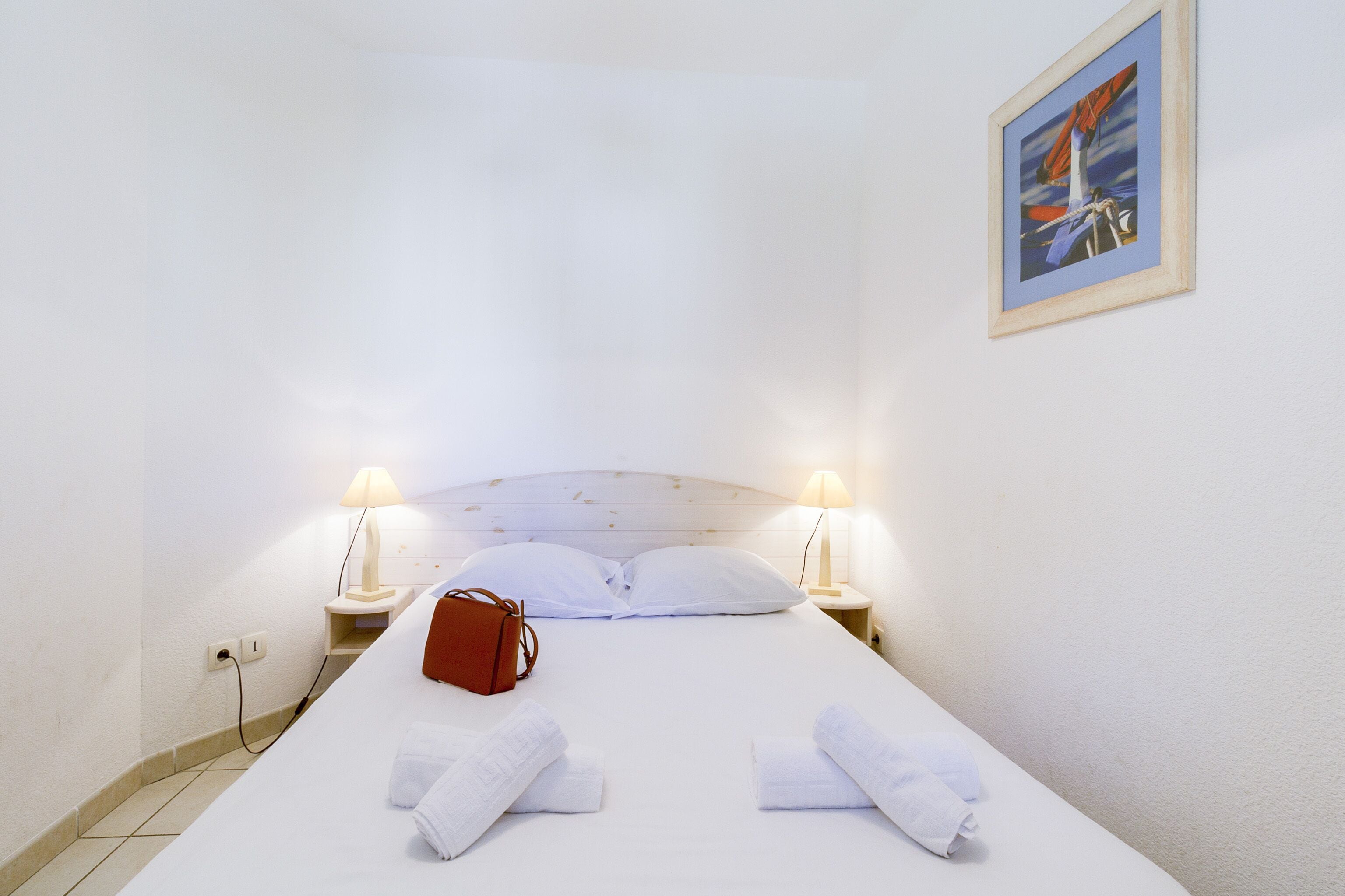 Ein ordentlich bezogenes Bett mit weißen Laken, einer roten Tasche und zwei Nachttischlampen.