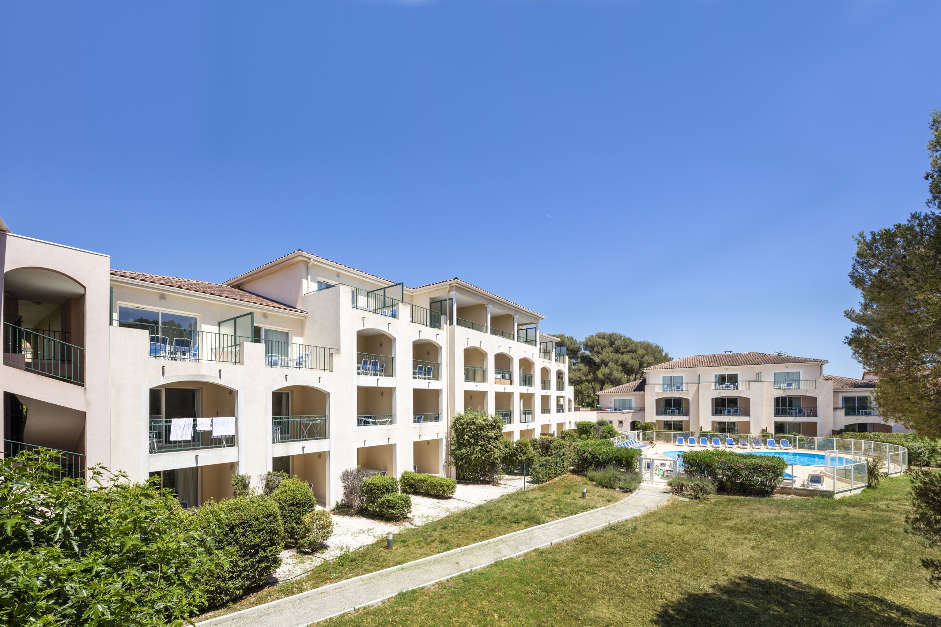 Un hôtel à plusieurs étages doté de balcons, d’une piscine et d’une pelouse bien entretenue.