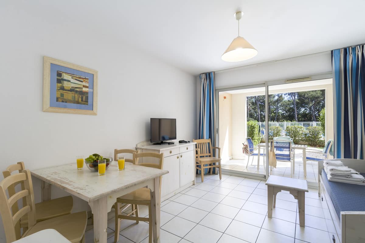 Una habitación con una mesa de comedor, sillas, un televisor y un amplio ventanal con cortinas.