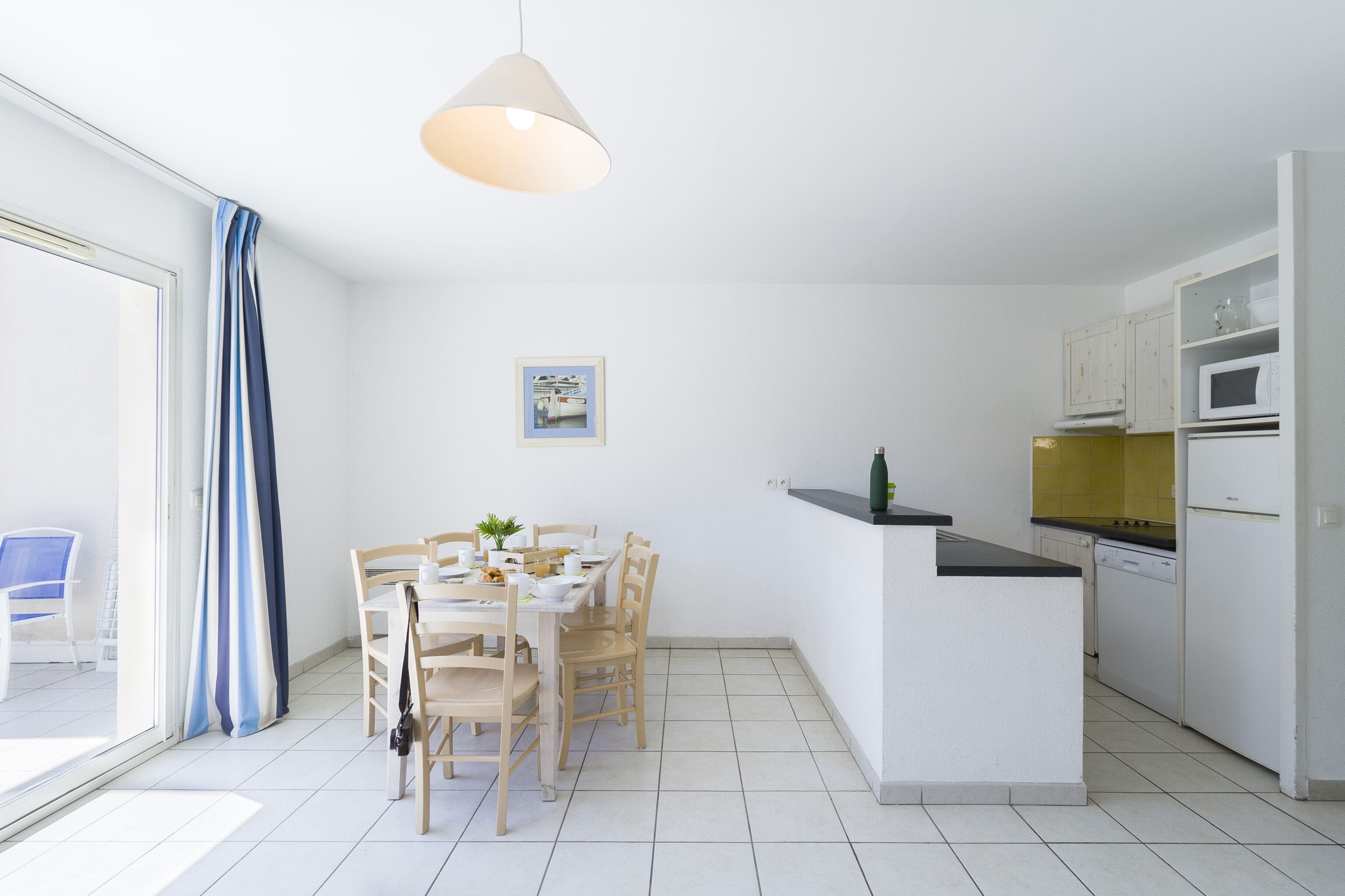 A modern kitchen with white cabinets, a microwave, and a dishwasher. There is a dining table with chairs and a hanging light fixture.