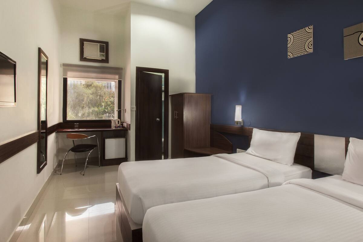 A hotel room with two beds, a desk, a chair, and a wardrobe.