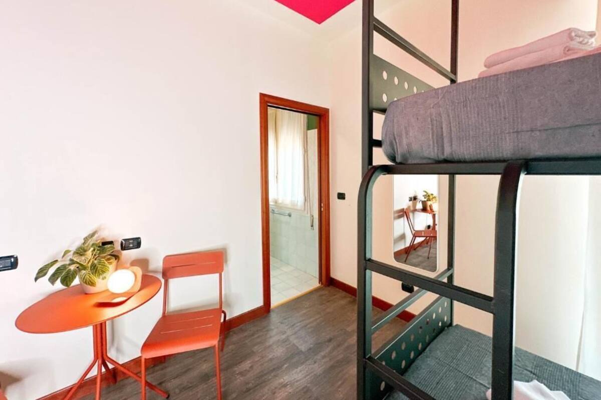 A bunk bed room with a small table and chair, a potted plant, and a door leading to another room.