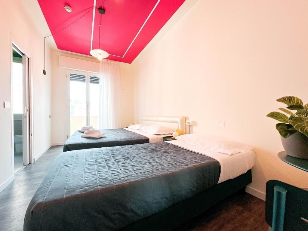 Habitación de hotel con dos camas, techo rojo, una planta en maceta y vistas al exterior.