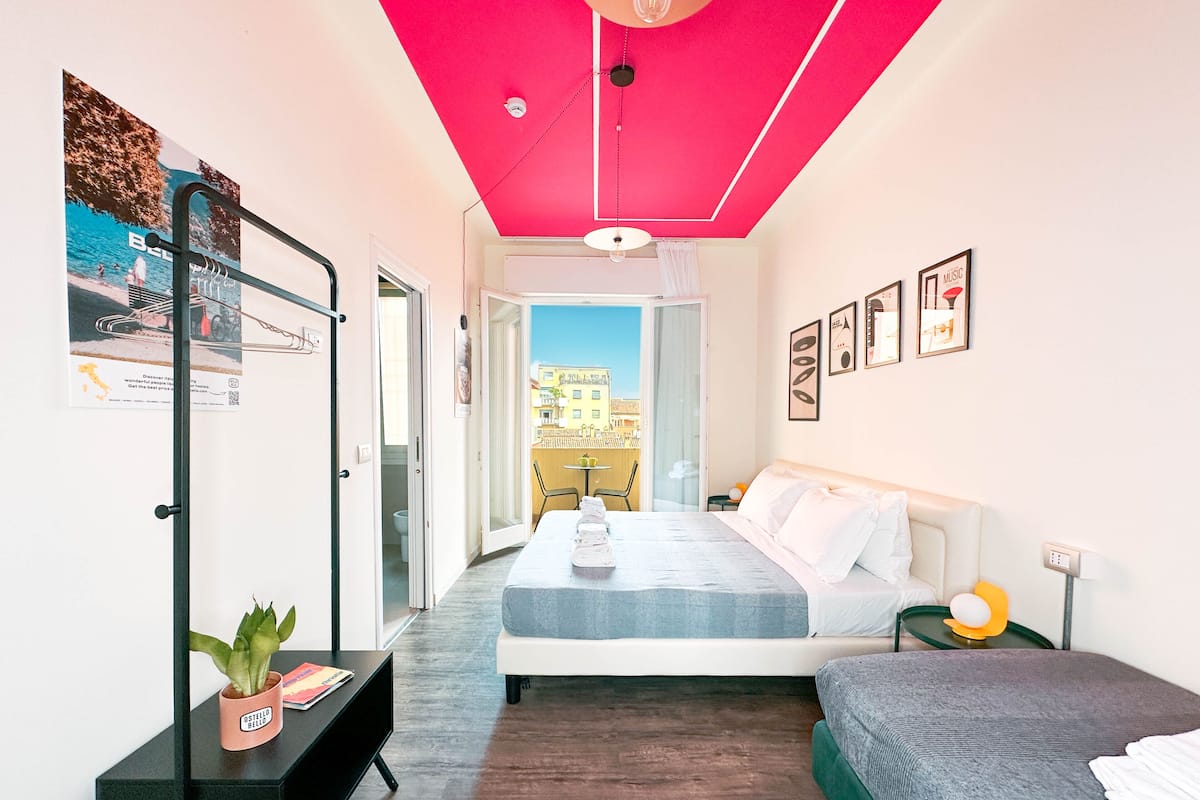 A modern hotel room with a bed, a sofa, a small table, and a potted plant.