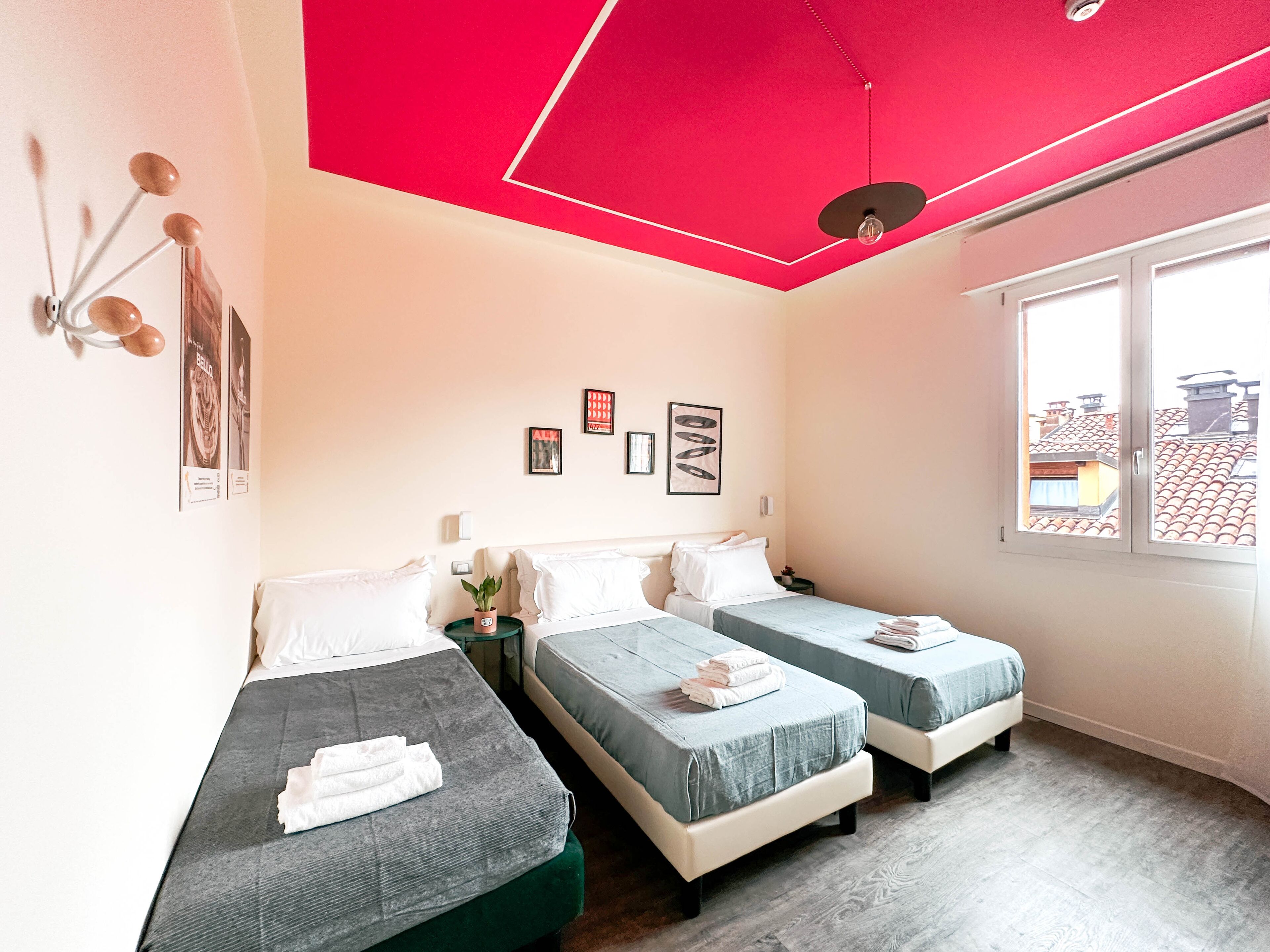 Une chambre d’hôtel avec deux lits simples, une grande fenêtre et un plafond rouge.