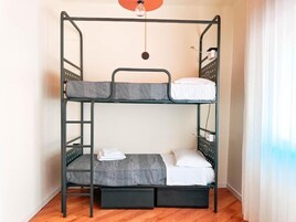 Een stapelbed met twee niveaus, elk voorzien van een matras en kussens. Er is een klein plankje onder het onderste bed en een hanglamp erboven.