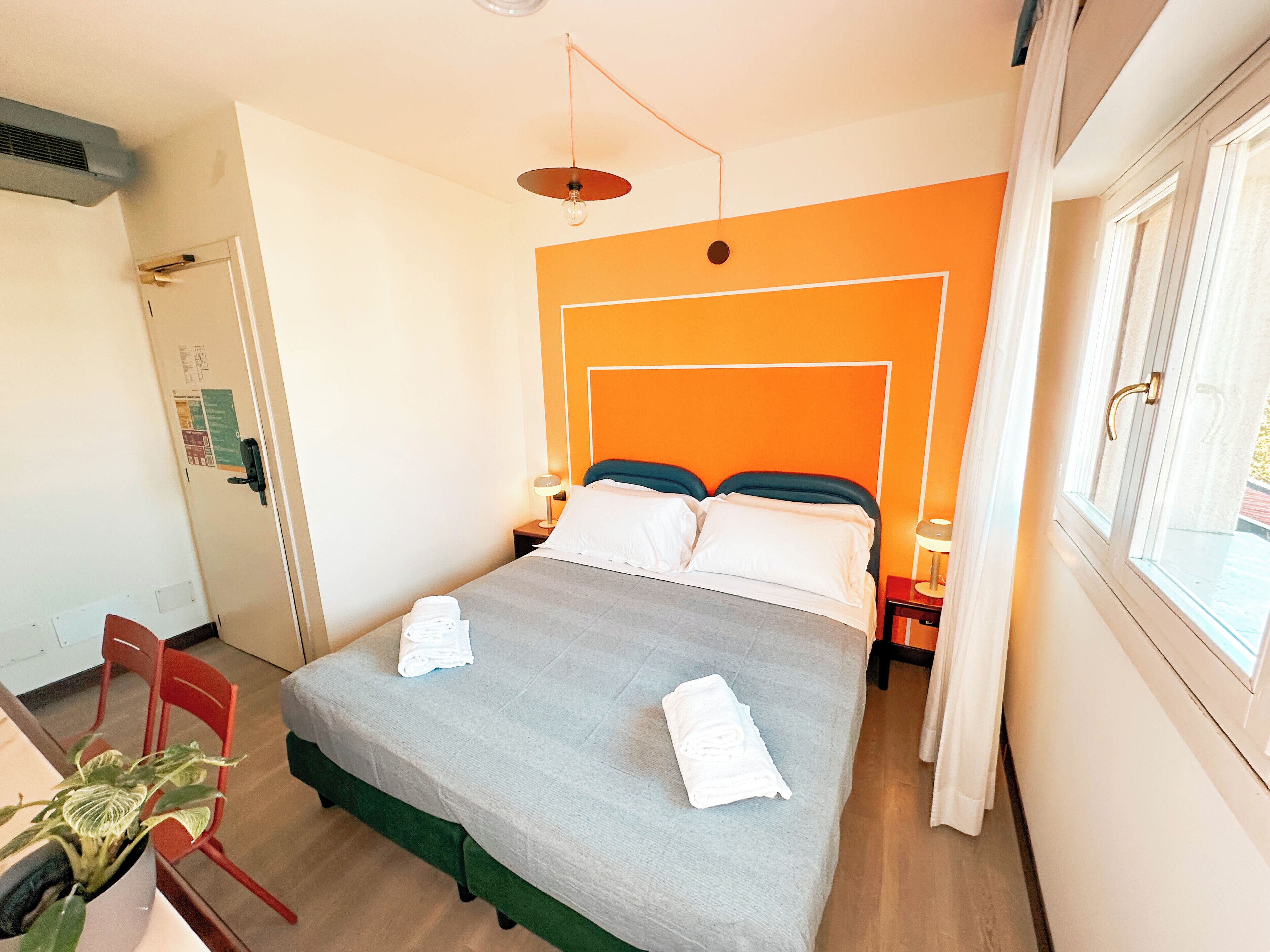 Una camera d'albergo con un letto, una scrivania, una sedia, una pianta in vaso e una finestra.