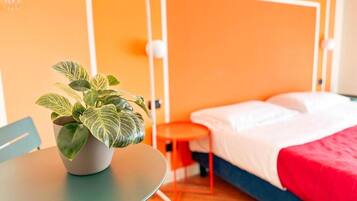 A hotel room with a bed, a small table with a plant, and a chair.