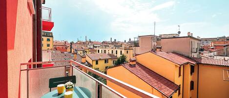 Un balcón con mesa y sillas, con vista a un paisaje urbano de edificios con tejados de tejas rojas.
