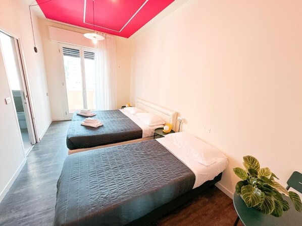 A hotel room with two beds, a potted plant, and a sliding door leading to a balcony.