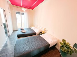 Una habitación de hotel con dos camas, una planta en maceta y un ventanal corredero que da a un balcón.
