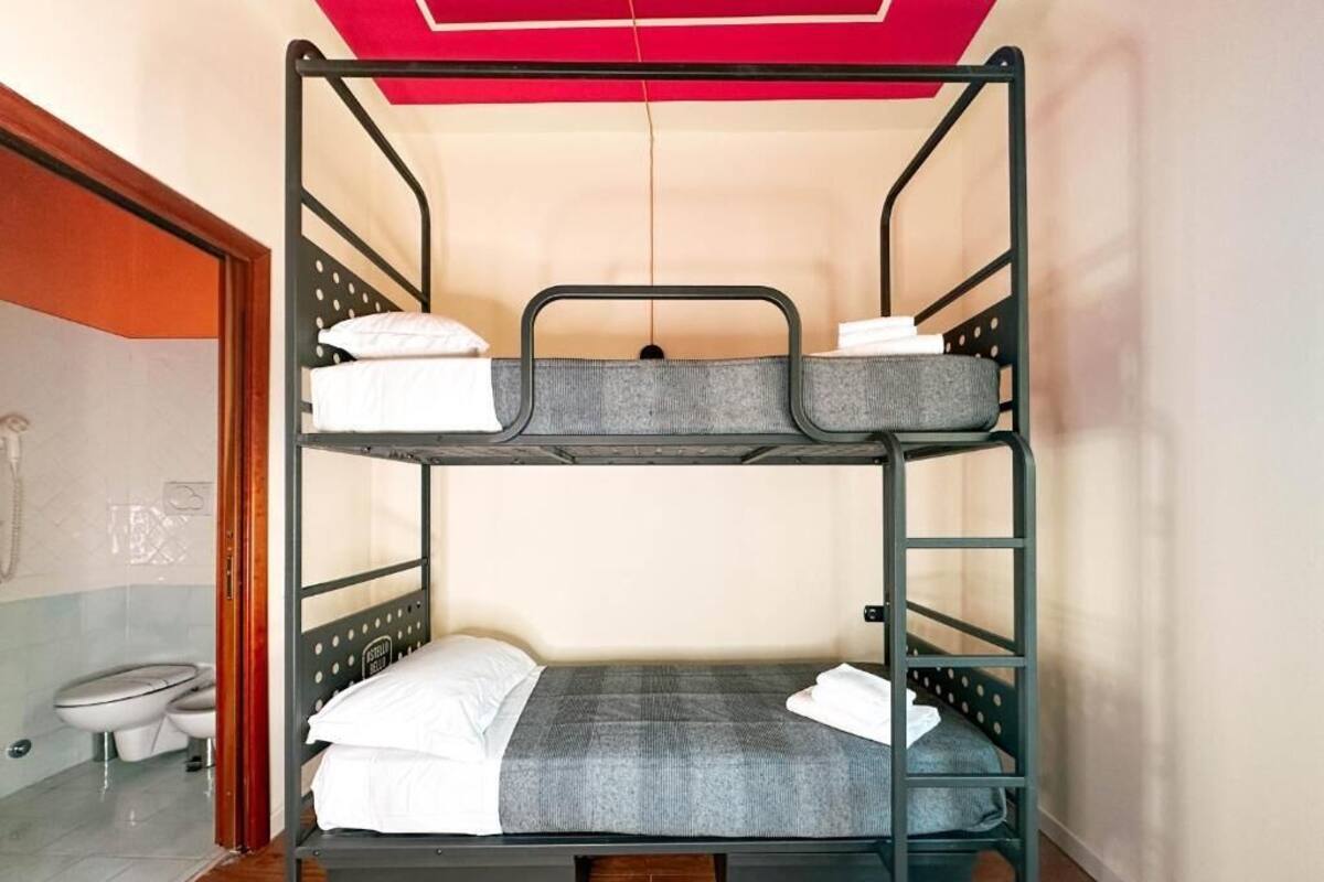 A bunk bed with a grey mattress and white bedding in a room with a wooden floor and a red ceiling.