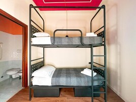 Una cama individual con colchón gris y ropa de cama blanca en una habitación con piso de madera y techo rojo.