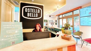 Aula, jossa on kyltti, jossa lukee ”OSTELLO BELLO”, sisään- ja uloskirjautumisaikataulu, Wi-Fi-tiedot ja ruokalista.