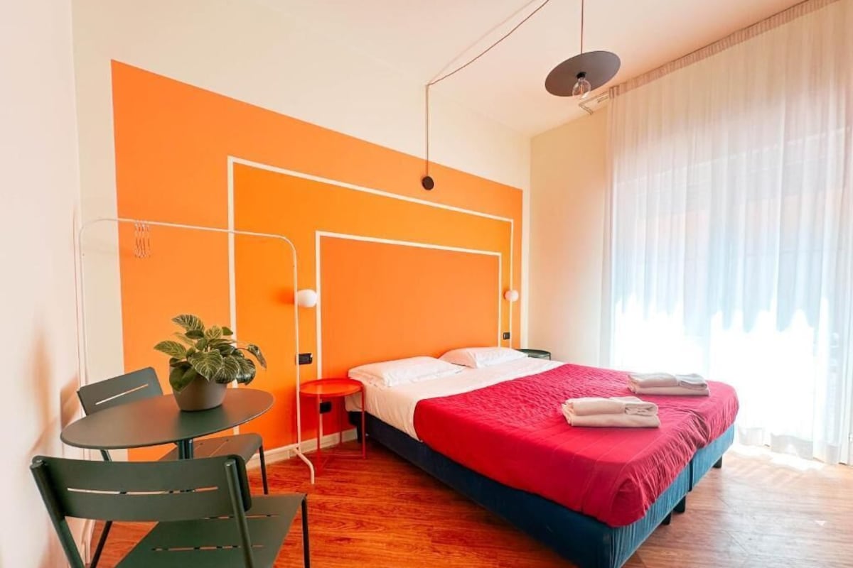Una habitación de hotel con una cama, una mesita con una planta, una silla y una mesita de noche.
