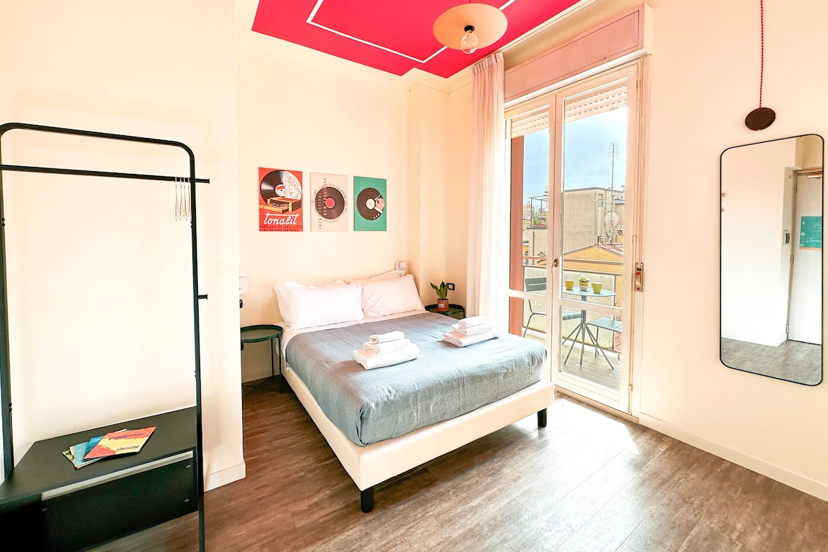 Un dormitorio con cama, escritorio, ventana y balcón.