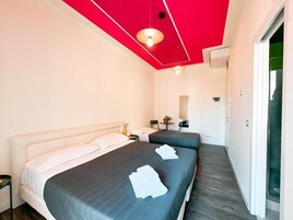 Habitación de hotel con dos camas, techo rojo, una mesita con una planta y una puerta a la derecha.