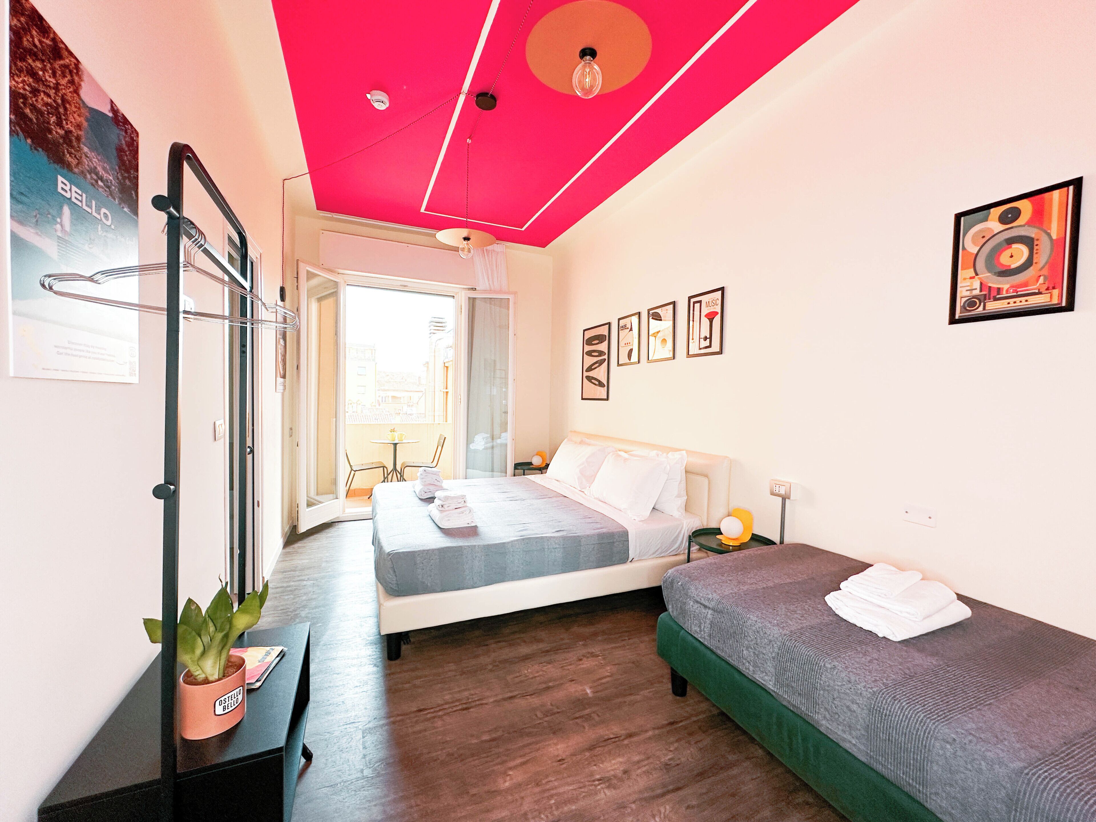 A bedroom with a bed, a smaller bed, a desk, a chair, a potted plant, and a balcony with a table and chairs.