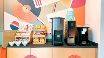 Una estación de café con una máquina de café, dispensador de agua y una exhibición de frutas.