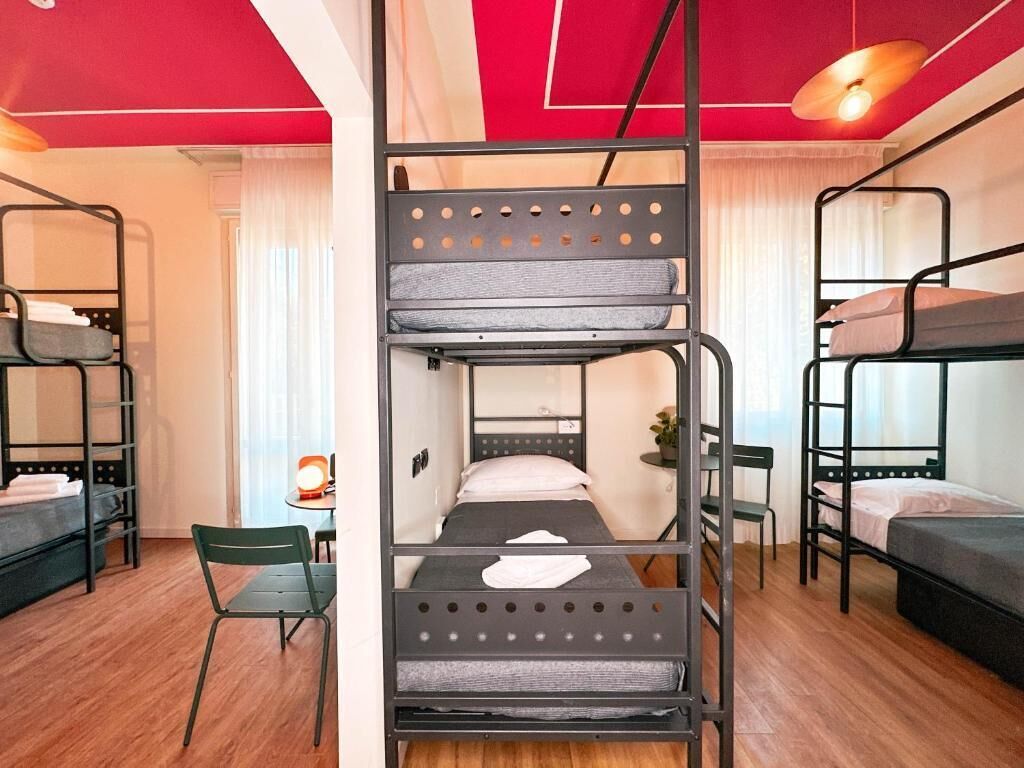 Un dormitorio con literas, una pequeña mesa con una silla y una ventana con cortinas.