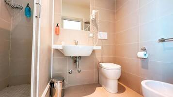 A bathroom with a shower, sink, toilet, and bidet.