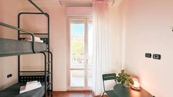 A room with bunk beds, a table with a plant, and a view through a window.