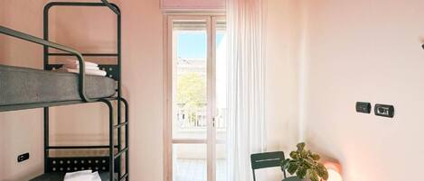 A room with bunk beds, a table with a plant, and a view through a window.