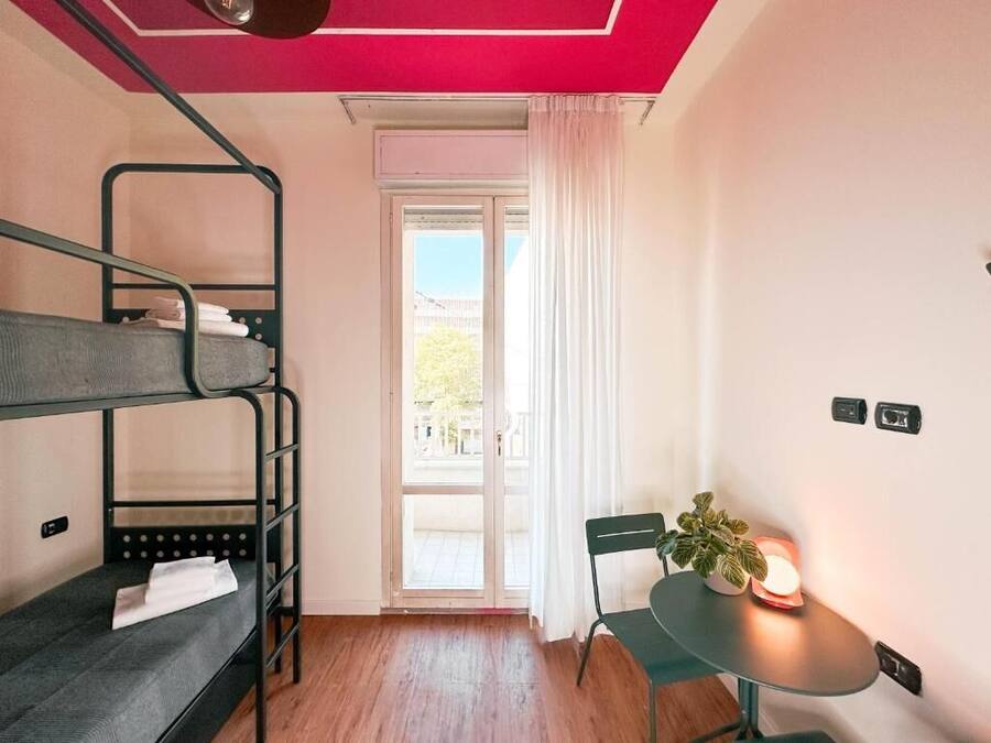 A room with bunk beds, a table with a plant, and a view through a window.