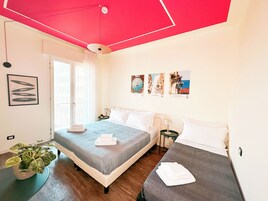 Ein Hotelzimmer mit einem Bett, einem Nachttisch, einer Lampe, einer Topfpflanze und einem Fenster mit Vorhängen.