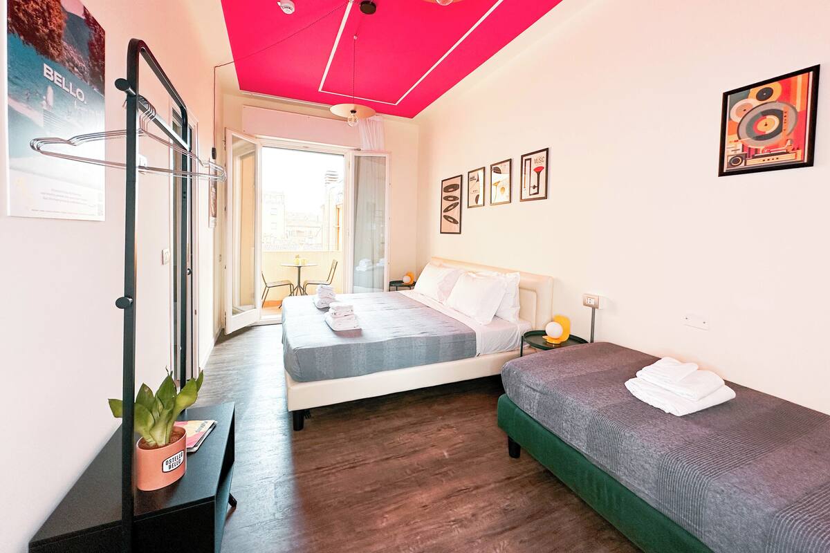 A bedroom with a bed, a smaller bed, a desk, a chair, a potted plant, and a balcony with a table and chairs.