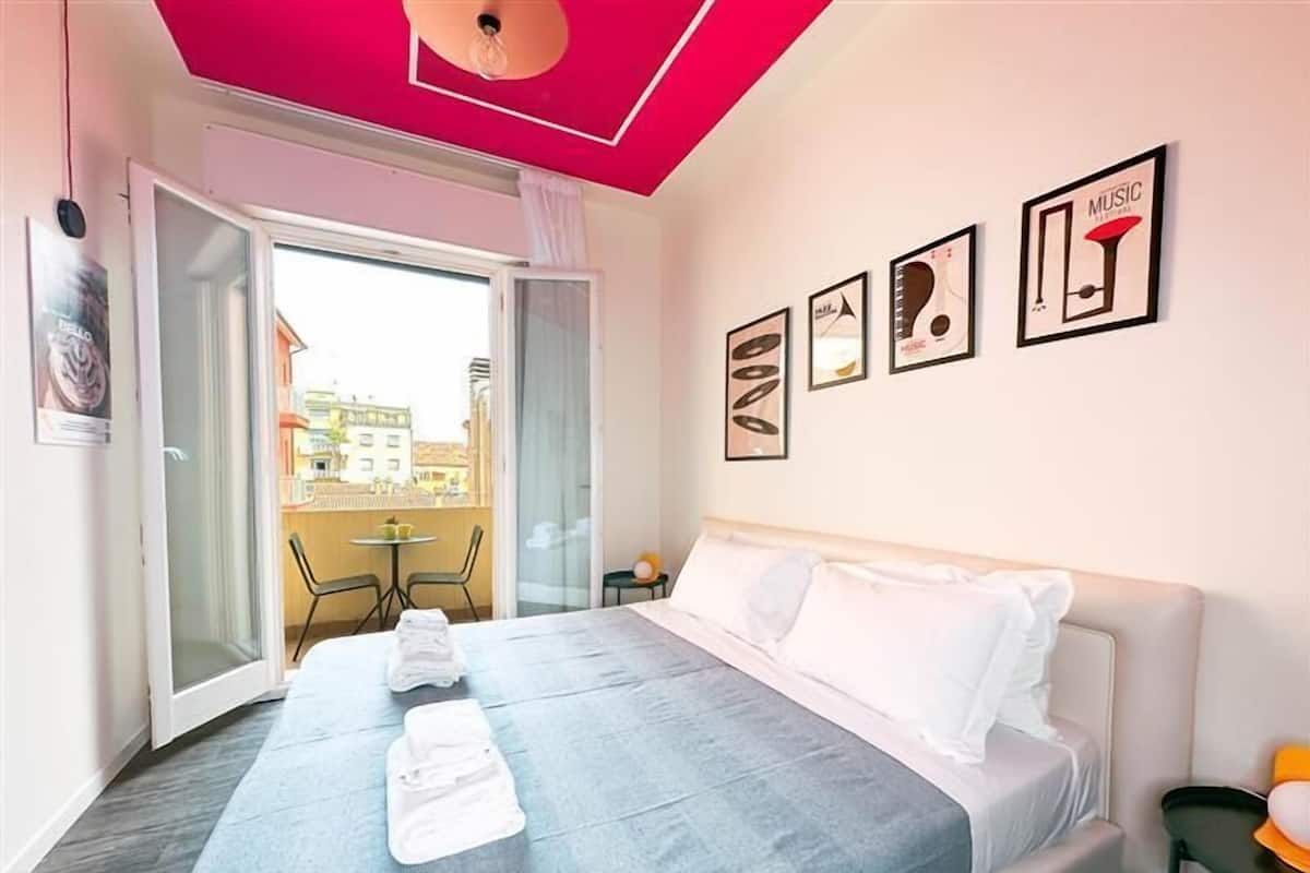 A hotel room with a bed, a balcony, and a view of buildings outside.