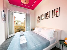 A hotel room with a bed, a balcony, and a view of buildings outside.